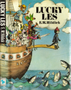 Okładka gamebooka "Lucky Les" autorstwa E. W. Hildicka. Przedstawia tytułowego kota Lesa wypychanego ze statku przez kotów-piratów na głębiny morskie, w których pływają rekiny.